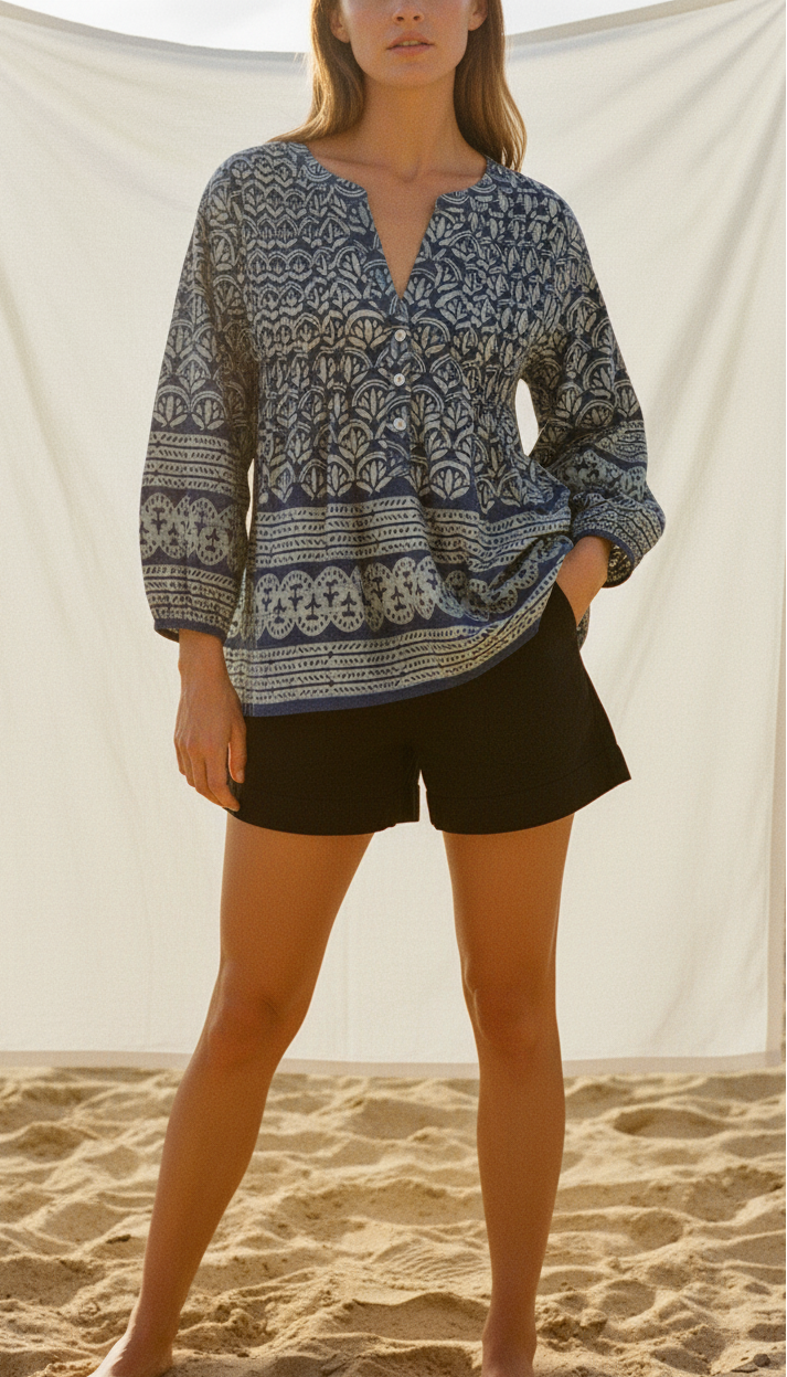 Woman wearing a patterned blouse and black shorts on a sandy background