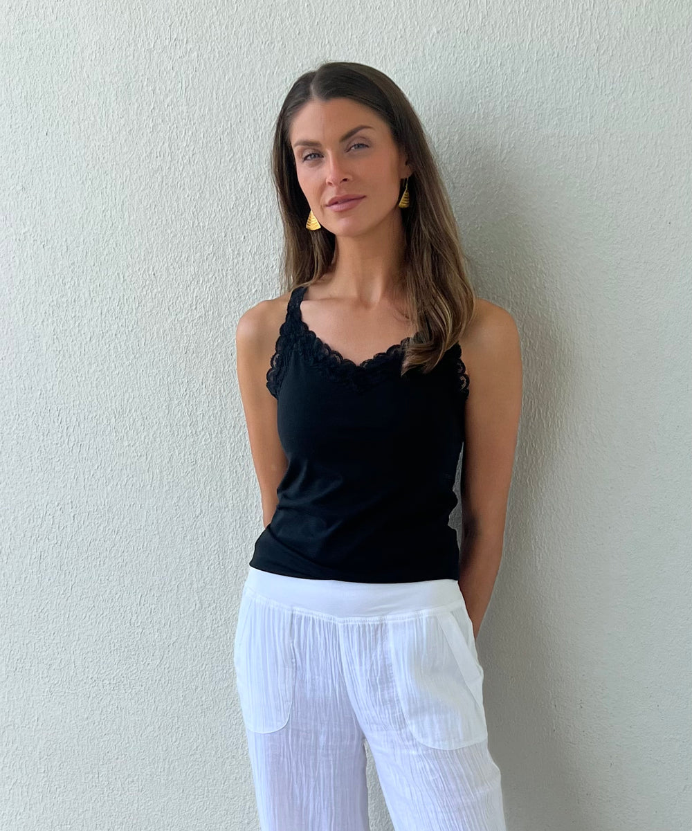 Woman wearing a black top and white pants against a plain wall