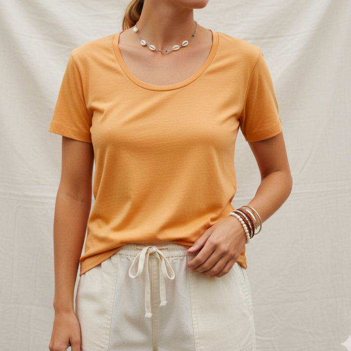 Person wearing a cotton mustard yellow t-shirt and white pants against a neutral background