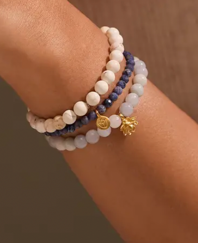 Three beaded bracelets with gold charms on a wrist against a neutral background