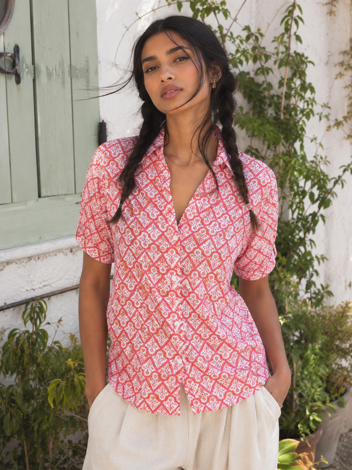 Woman wearing a pink patterned shirt and white pants standing outdoors.
