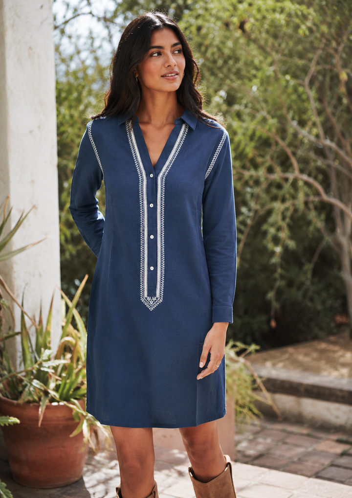 Woman wearing a blue dress with white embroidery standing outdoors.