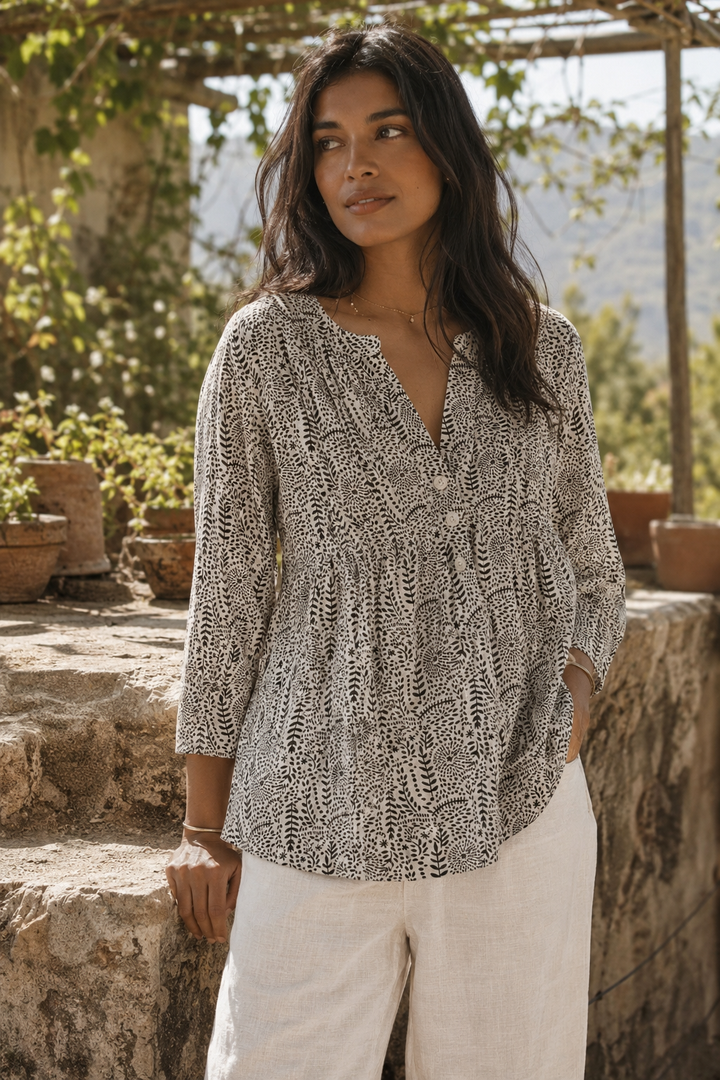 Woman wearing a cotton patterned blouse and white pants standing outdoors with greenery in the background