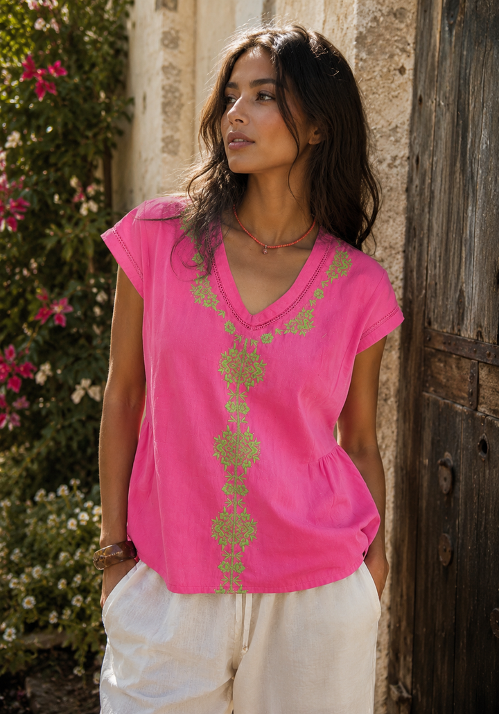 Woman wearing a bright pink top with green patterns against a rustic background