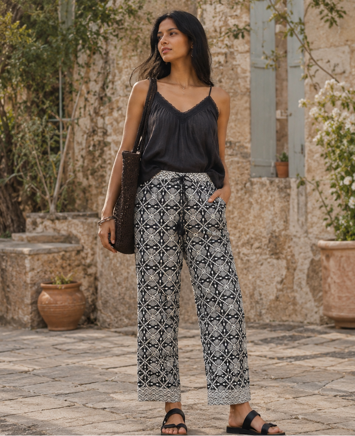 Woman wearing a black top and patterned pants standing in an outdoor setting.