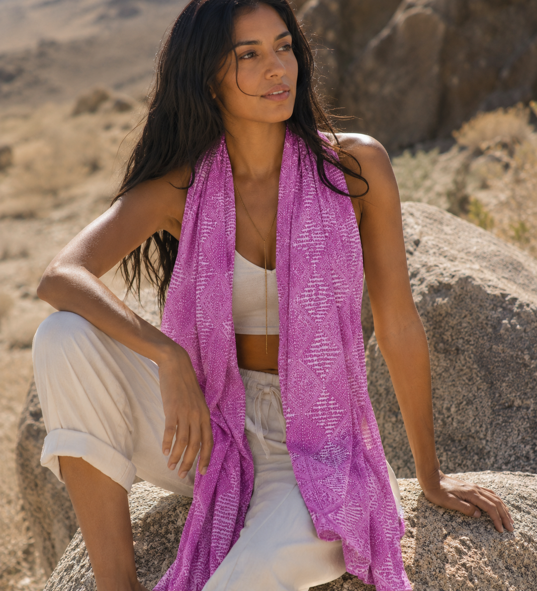 Woman sitting on a rock in a desert-like setting wearing a purple scarf.