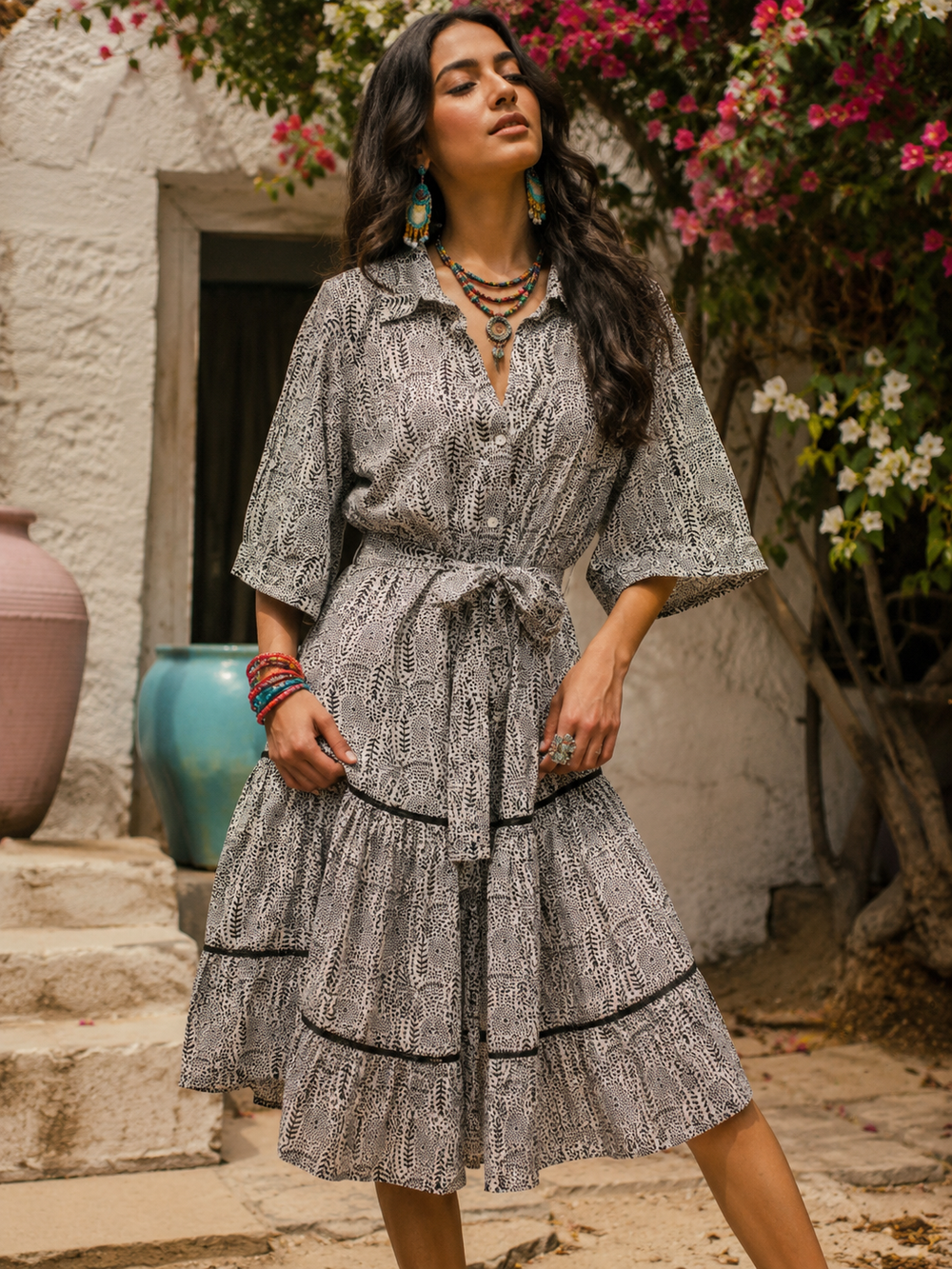 Woman in a patterned dress standing in front of a white wall with flowers.