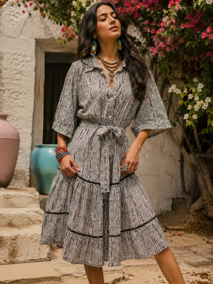 Woman in a patterned dress standing in front of a white wall with flowers.