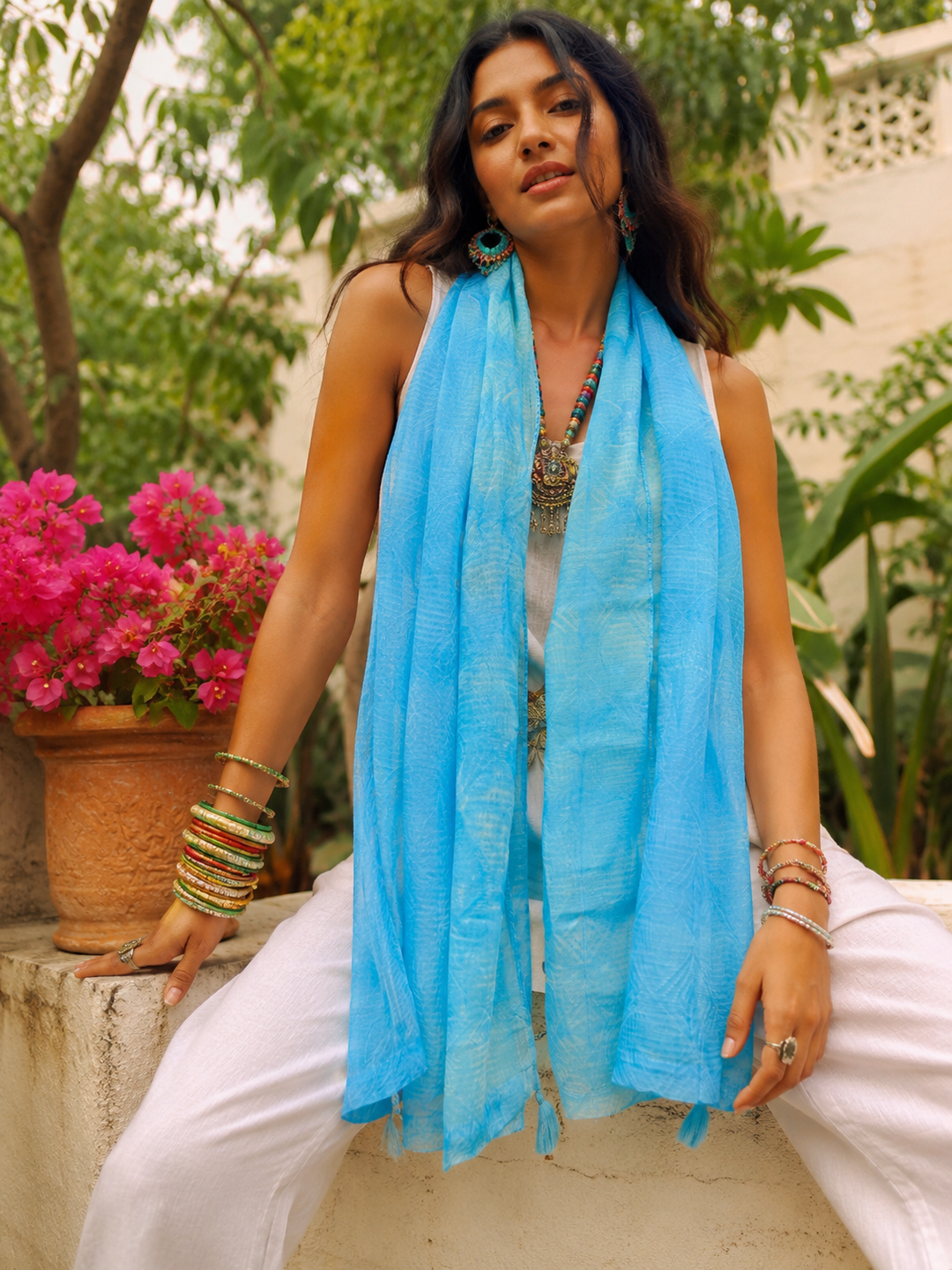 Woman wearing a blue scarf sitting outdoors with plants and flowers in the background