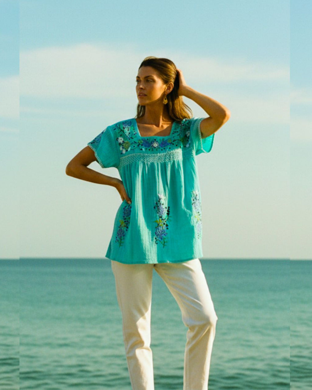 Woman in a turquoise top and white pants standing by the ocean