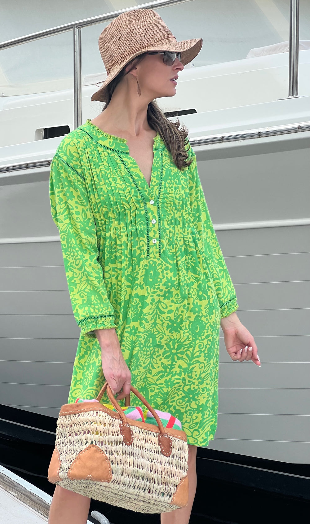 Woman in a green dress and straw hat standing in front of a boat.