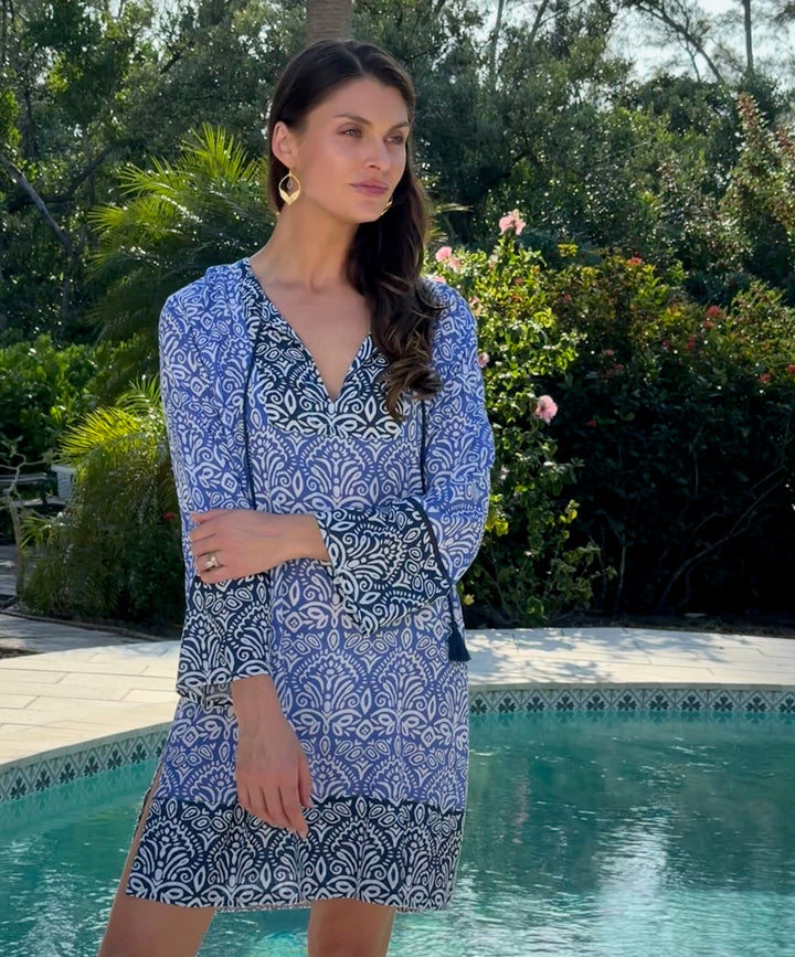 Woman in a blue and white patterned dress standing by a pool with greenery in the background