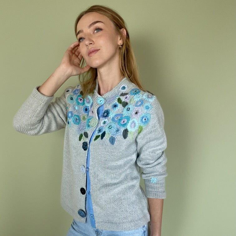 Woman wearing a gray cardigan with floral embroidery on a plain background