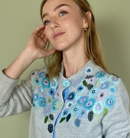 Woman wearing a sweater with floral embroidery against a plain background