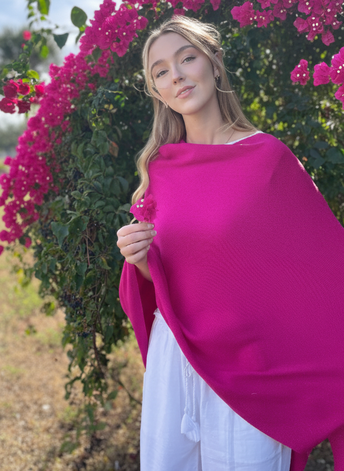 Woman wearing a bright pink shawl in front of a flowering bush