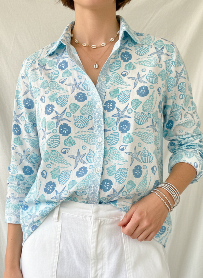 Person wearing a light blue shell print shirt and white pants on a plain background
