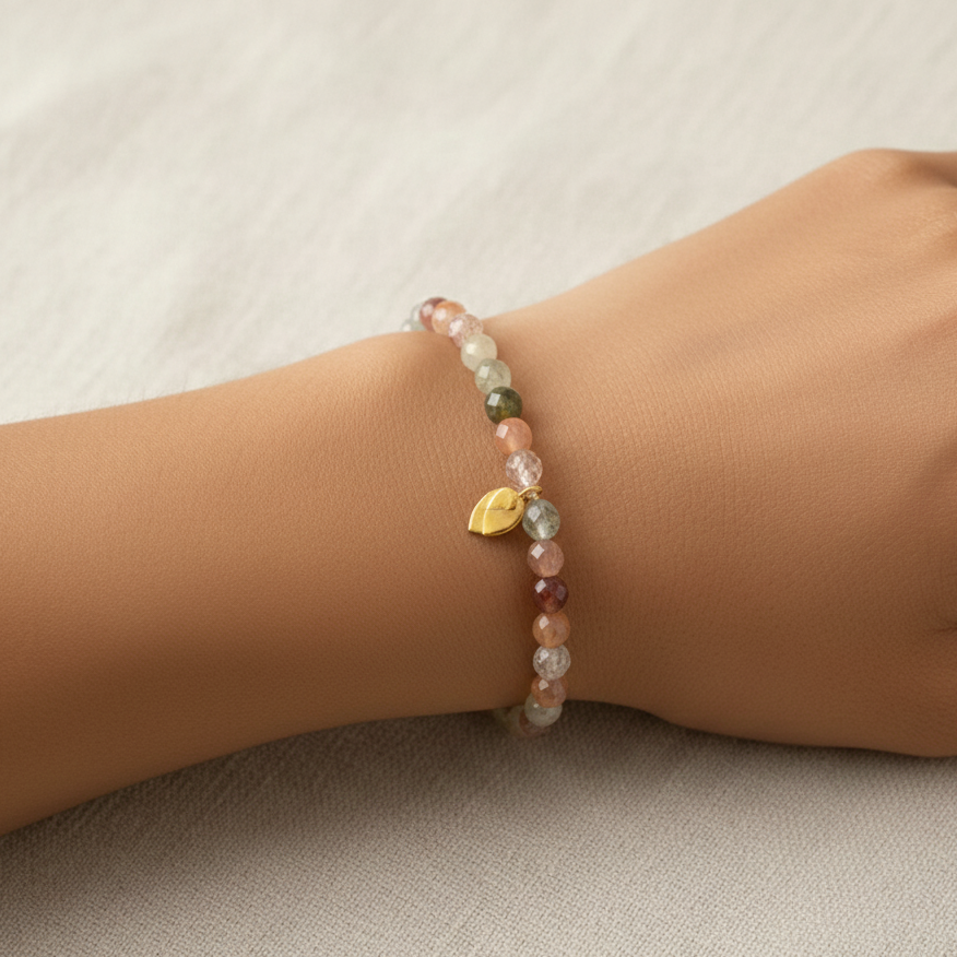 Multicolored beaded bracelet with a gold leaf charm on a wrist against a neutral background