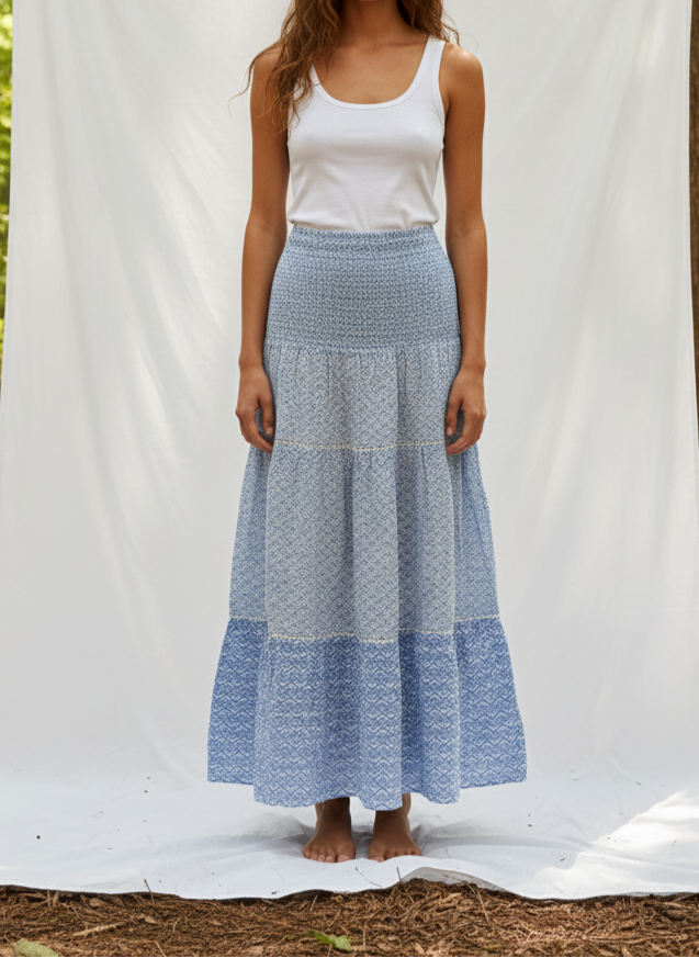 Woman wearing a long blue patterned skirt over a white tank top against a white backdrop.