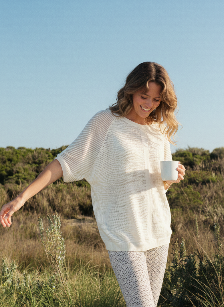 Woman in a cotton sweater holding a mug in a field with a clear blue sky.