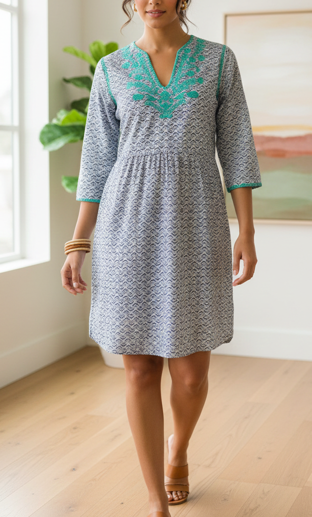 Woman wearing a patterned dress with teal embroidery in a room with a painting and plant.