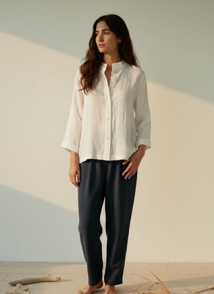 Woman wearing a white shirt and dark pants standing in a minimalistic setting with a neutral background.