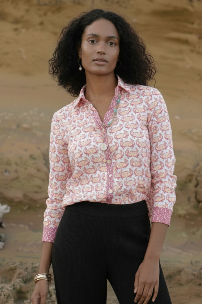 Woman wearing a patterned blouse and black pants against a natural background