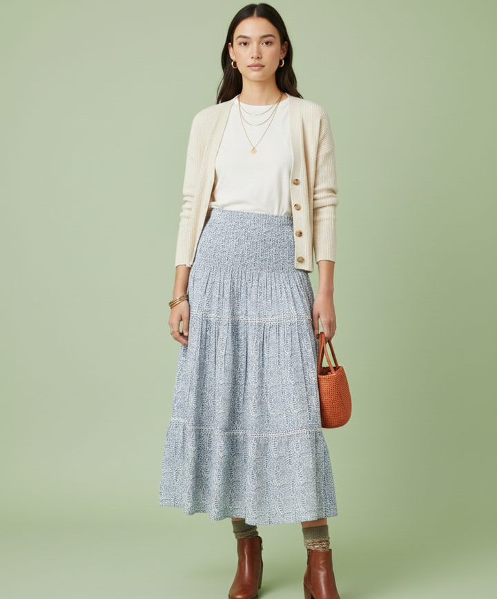 Woman wearing a beige cardigan, white top, and blue tiered skirt on a green background