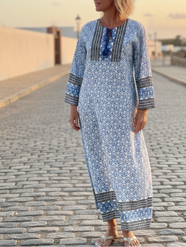 Woman wearing a long blue dress with patterns standing on a cobblestone street.