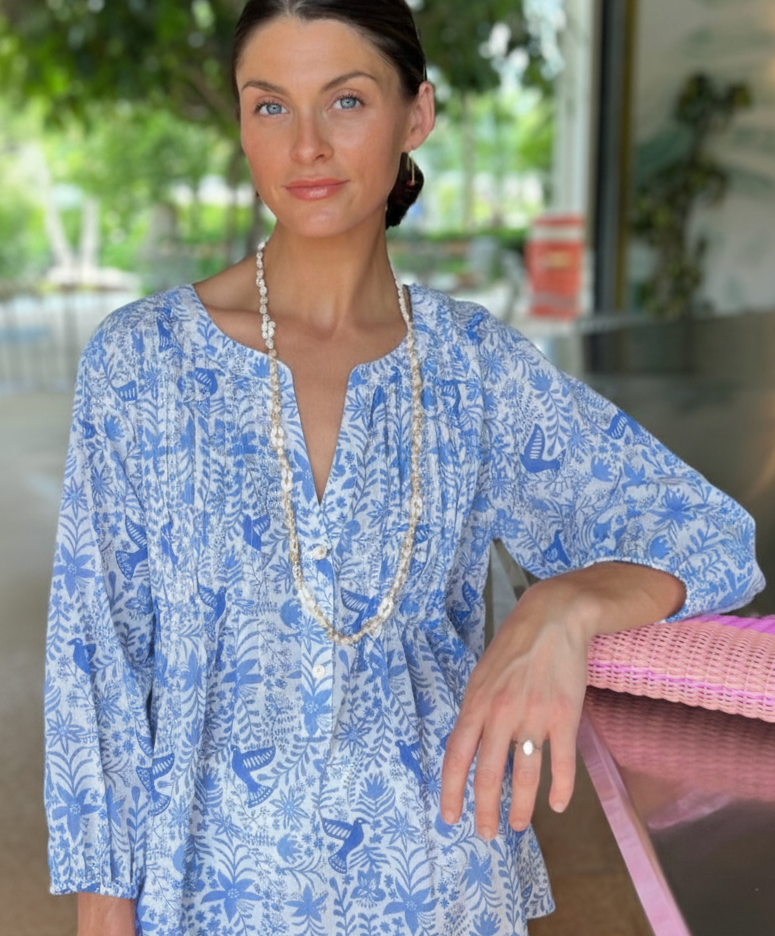 Woman wearing a blue floral blouse with a pink clutch in an indoor setting