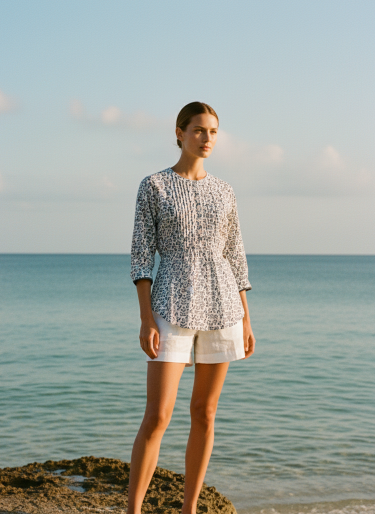 Woman standing on a rock by the ocean wearing a patterned top and shorts.