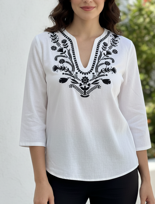 Woman wearing a white blouse with black embroidery outdoors.