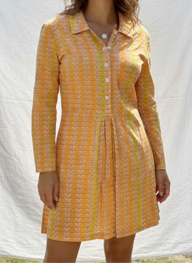 Woman wearing a yellow patterned dress standing against a white backdrop outdoors.