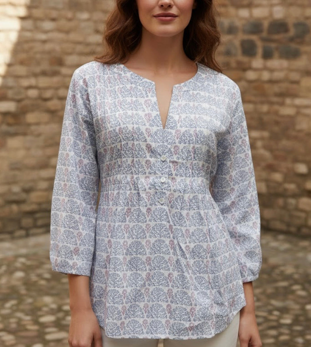 Woman wearing a patterned blouse against a stone wall.