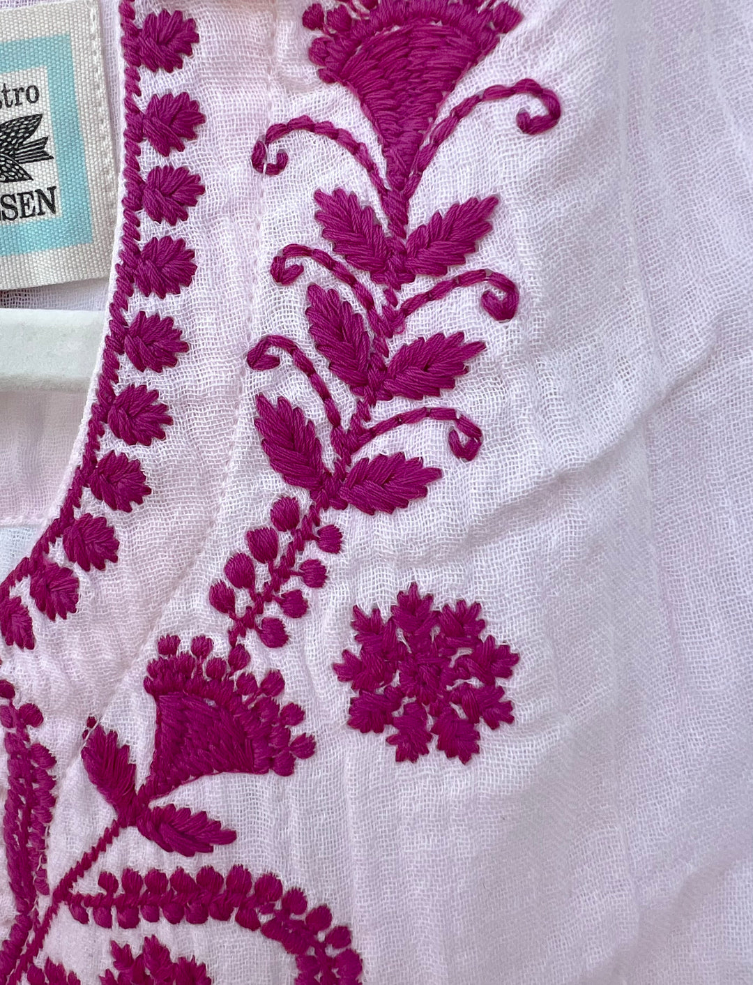 Close-up of white fabric with intricate purple floral embroidery.
