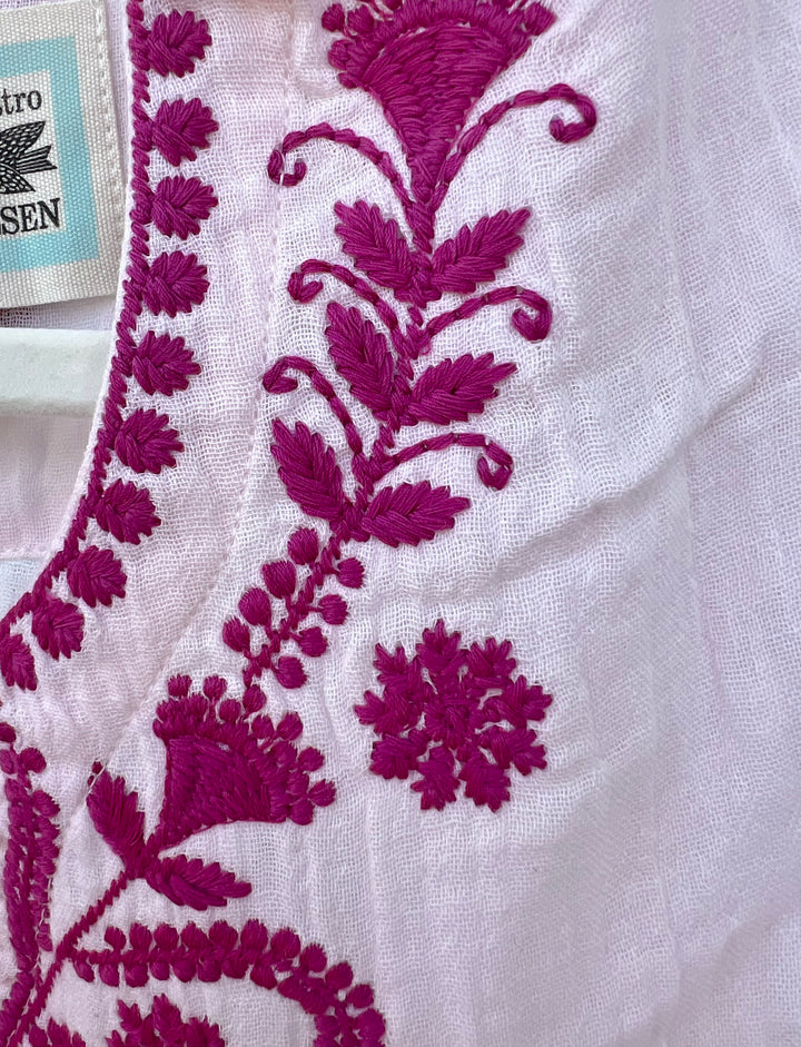 Close-up of white fabric with intricate purple floral embroidery.
