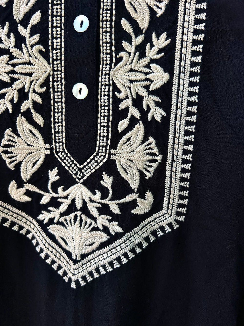 Close-up of a black garment with intricate white embroidery