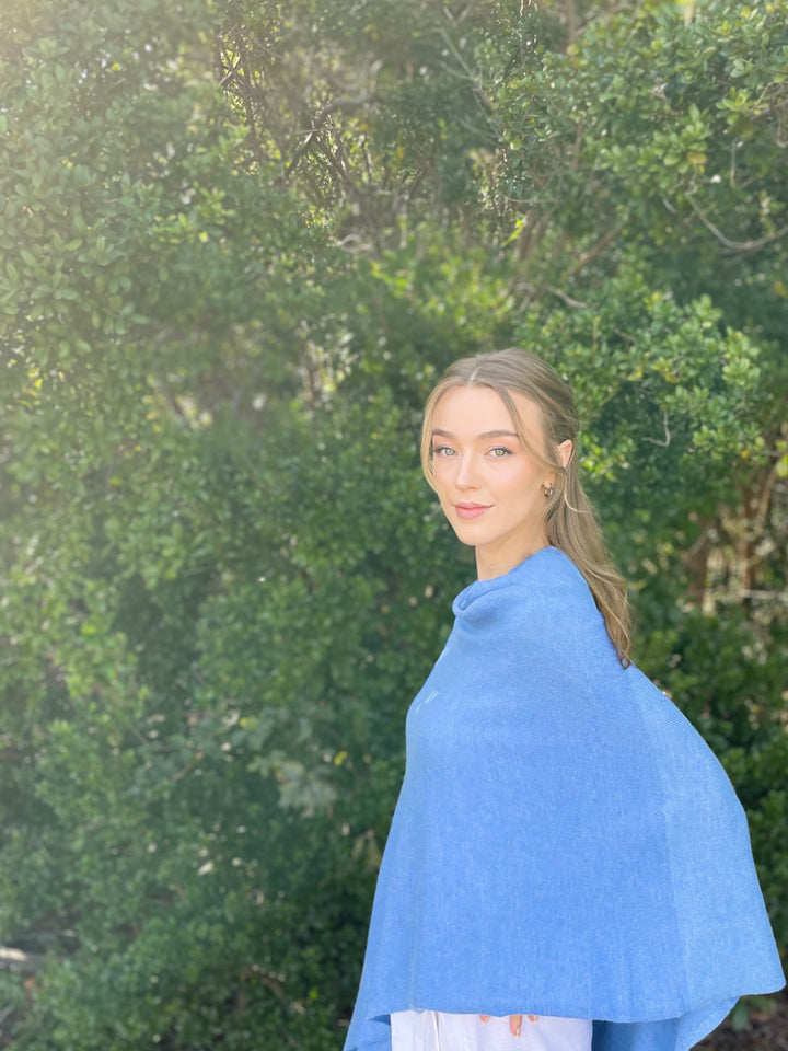 Woman wearing a blue shawl outdoors with greenery in the background