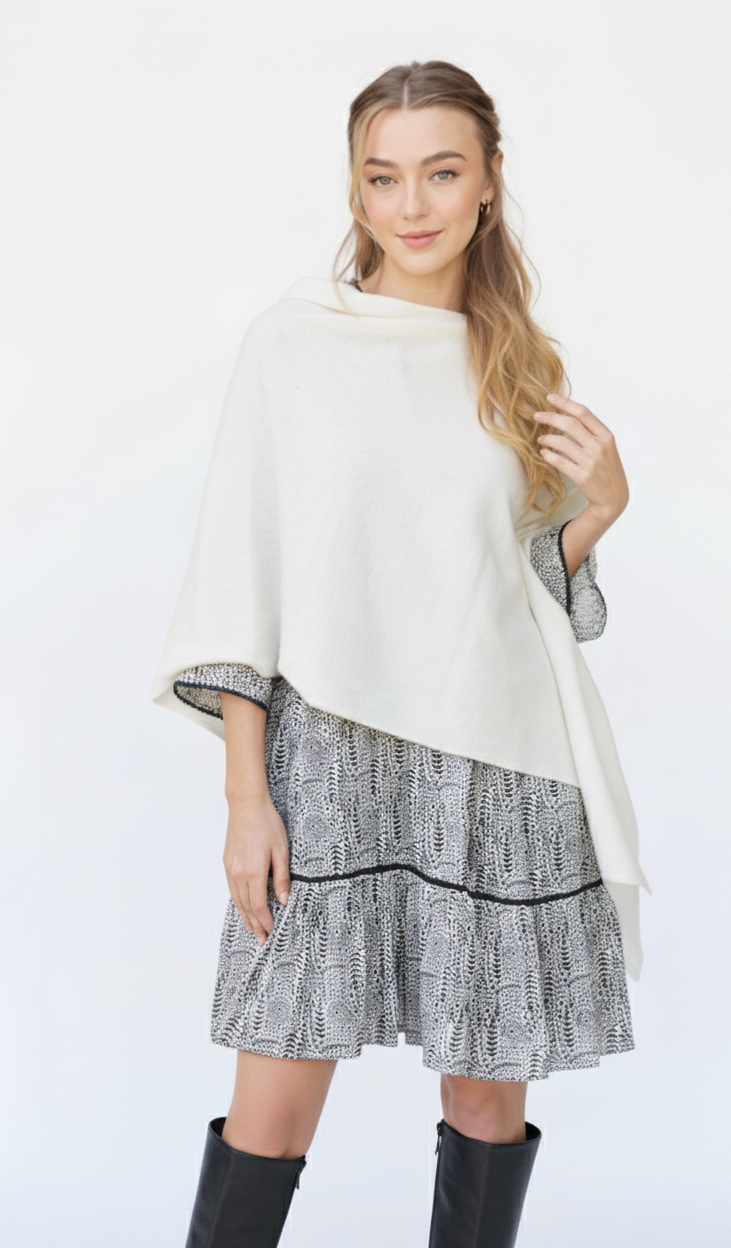 Woman wearing a white cashmere poncho over a patterned dress on a white background