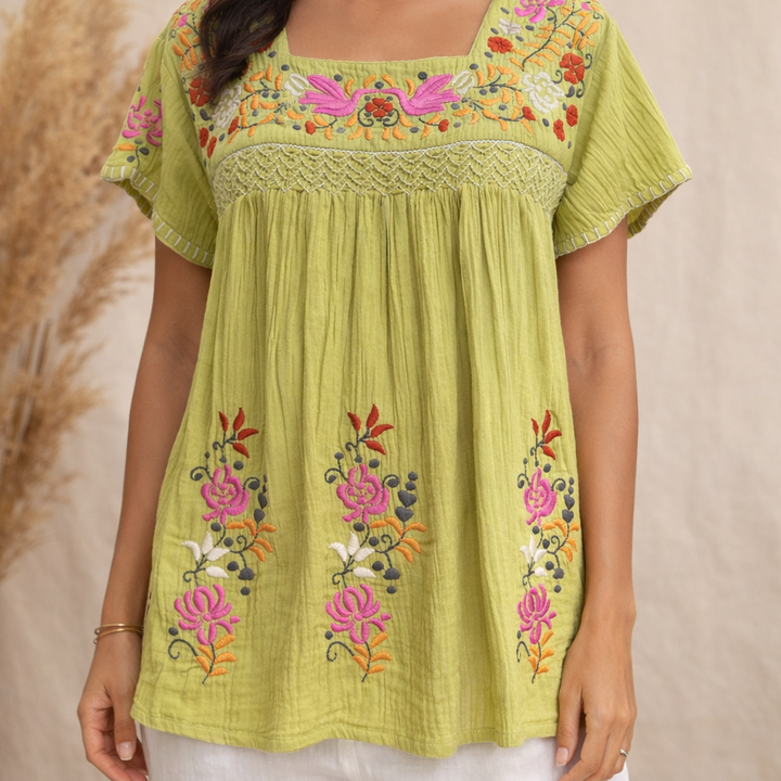 Green embroidered top with floral patterns on a neutral background